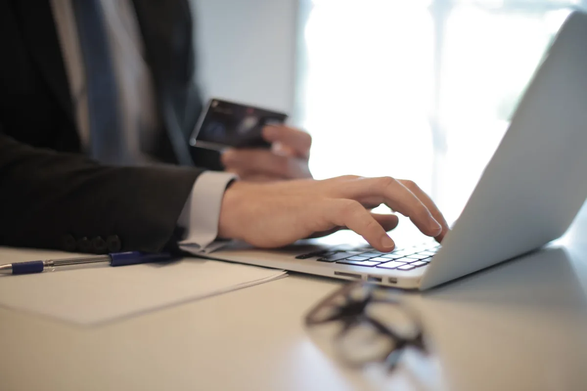 person typing on laptop with credit card on desk