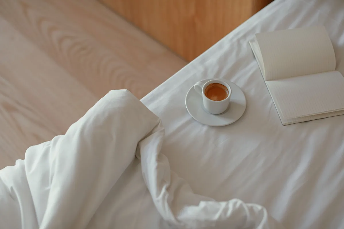 espresso cup next to a neatly made luxury hotel bed