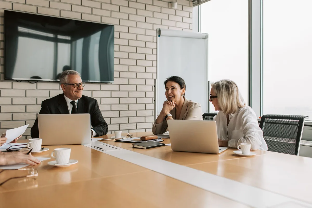corporate meeting room with attendees sitting around a conference table with coffee cups