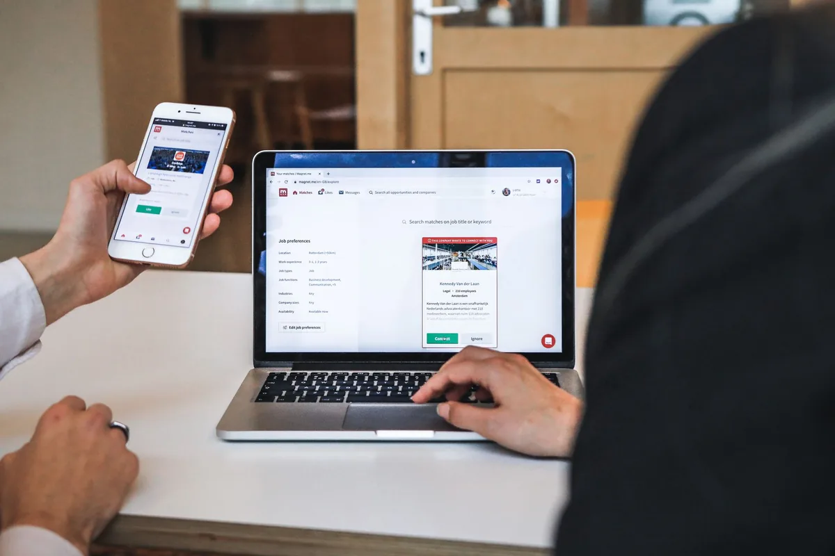 person typing on a smartphone with a hotel booking website visible on a laptop in the background