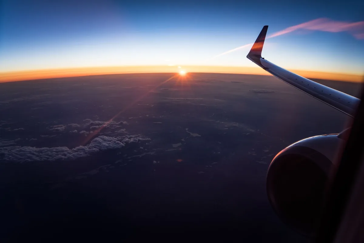 airplane wing flying above clouds sunset